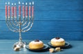 Silver menorah, dreidels with He, Pe, Nun, Gimel letters and sufganiyot on blue wooden table, space for text. Hanukkah symbols