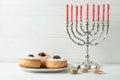Silver menorah, dreidels with He, Pe, Nun, Gimel letters and sufganiyot on white wooden table, space for text. Hanukkah symbols