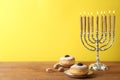 Silver menorah, dreidels with He, Pe, Nun, Gimel letters and sufganiyot on wooden table against yellow background, space for text