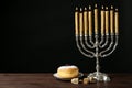 Silver menorah near sufganiyah and dreidels with symbols Nun, He, Pe, Gimel on black background. Space for text Royalty Free Stock Photo