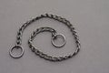 Silver metal chain with two rings on a gray background. Tugging dog leash