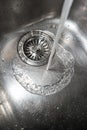 Silver metal kitchen sink close up shot with running tap water near the drain top view Royalty Free Stock Photo