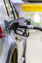 Silver mettalic color car refueling on public gas station - close-up with selective focus and blurry background