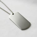 Silver military dog tag on a ball chain necklace lies on a white fabric surface. The tag is Royalty Free Stock Photo