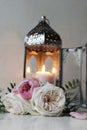 Silver Moroccan, Arabic lantern with burning candle. Pink roses flowers on white table. Festive still life for muslim