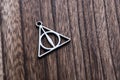 Silver necklace of deathly hallows on wood background. Symbol of harry potter fans