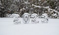 Silver numbers of the New Year 2023 in winter in the snow on the background of snow-covered trees and bushes with copy space