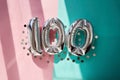 Silver numbers 100 one hundred years balloons in sunlight pink turquoise background Royalty Free Stock Photo