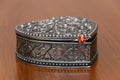 Silver ornate heart jewelry box on wood table with red ring