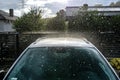 A silver passenger car parked in the driveway in front of the garage in the pouring rain during a downpour.