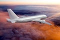 Silver passenger plane flies away. The plane flies over the pink sunset clouds. Rear view of aircraft