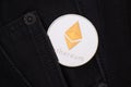 A silver physical Ethereum coin with golden symbol sticks out of the pocket of black jeans close-up. Royalty Free Stock Photo