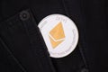 A silver physical Ethereum coin with golden symbol sticks out of the pocket of black jeans close-up. Royalty Free Stock Photo