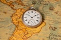 Silver retro pocket watch lying on a paper old world map. Antique round clock with a dial and arrows on a geographical