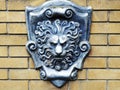 A silver shield with a basrelief lion's head on a yellow brick wall