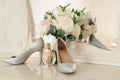 Silver shoes of the bride , perfume, bouquet and wedding rings on the dressing table near the mirror.