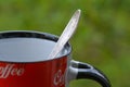 Silver spoon in red coffee mug on green background Royalty Free Stock Photo