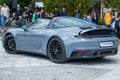 A silver sports Porsche with some people watching it in the background