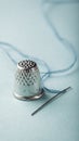 Silver thimble and needle with blue thread on soft pastel background for sewing enthusiasts Royalty Free Stock Photo