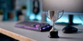 Silver trophy cup on desk with blurred gaming keyboard and mouse in modern illuminated workspace Royalty Free Stock Photo