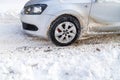 Silver vehicle moving on snowy road skidding, car's wheel spin and throw out pieces of snow it attempts to gain traction