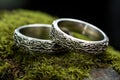 silver wedding bands nested on a mossy river stone