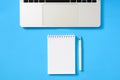 Silvery laptop and notepad with a blank white sheet on a blue background. Royalty Free Stock Photo