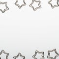 Silvery paper clips in the form of stars on a gray background. Frame of office stationery. Copy space, top view, flat