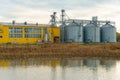 Silvery silos are reflected in the water. A modern grain storage, processing and drying plant against the background of the sky at Royalty Free Stock Photo