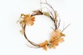 Simple autumn wreath hanging on white wall. Modern rustic autumn wreath made of branches, twig, fall leaves, dried herbs and