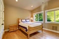 Simple beige bedroom with nightstand, hardwood floor and two windows.