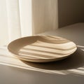 A simple beige ceramic plate sits on a smooth white table. Sunlight streams through Royalty Free Stock Photo