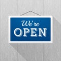 Simple blue sign with text `we`re open` hanging on a gray wooden wall.