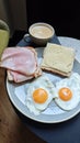 Simple breakfast plate with fried eggs, ham and cheese sandwiches, and a cup of coffee on a small table. The image represents Royalty Free Stock Photo
