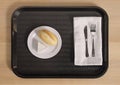 Simple breakfast tray with bread roll and white cheese served on black plastic cafeteria tray with silverware and folded white Royalty Free Stock Photo