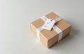 Simple brown gift box with white ribbon and check tag sits on light surface. Package ready for delivery or shipment. Cardboard Royalty Free Stock Photo