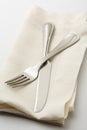 Simple, casual fine dining place setting with high quality silverware fork and knife on white linen napkin with white tablecloth