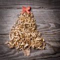 Simple Christmas tree arranged from sawdust, wood-chips on wooden background. Orange cute ribbon. Royalty Free Stock Photo