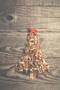 Simple Christmas tree arranged from sawdust, wood-chips on wooden background. Orange cute ribbon.