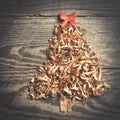 Simple Christmas tree arranged from sawdust, wood-chips on wooden background. Orange cute ribbon.