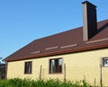 A simple construction brick house with brown metal roof, snow-guards and chimney against blue sky Royalty Free Stock Photo