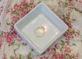 Simple gold solitaire engagement ring in white jewelry tray on v