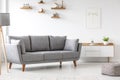 Simple, gray sofa standing next to a white cupboard in living room interior with decorations on wooden shelves. Real photo