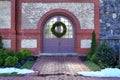 A simple, green Christmas holiday wreath hanging on a set of double doors with small piles of snow