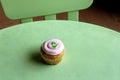 Simple green table and chair with one strawberry cupcake with thick, creamy frosting