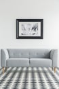 Simple, grey sofa on a checkered floor with a poster in the back