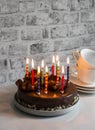 Simple homemade chocolate birthday cake with burning candles on the table. Holiday concept