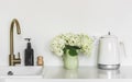 Simple kitchen interior in Scandinavian style. Sink with brass faucet, bouquet of hydrangeas in a ceramic jug, electric kettle,