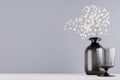 Simple minimalist spring interior in monochrome grey color - black glass drink and vase and bouquet of small flowers on white. Royalty Free Stock Photo