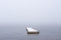 Simple minimalistic landscape image of single floating jetty on Loch Lomond during Winter snow fall